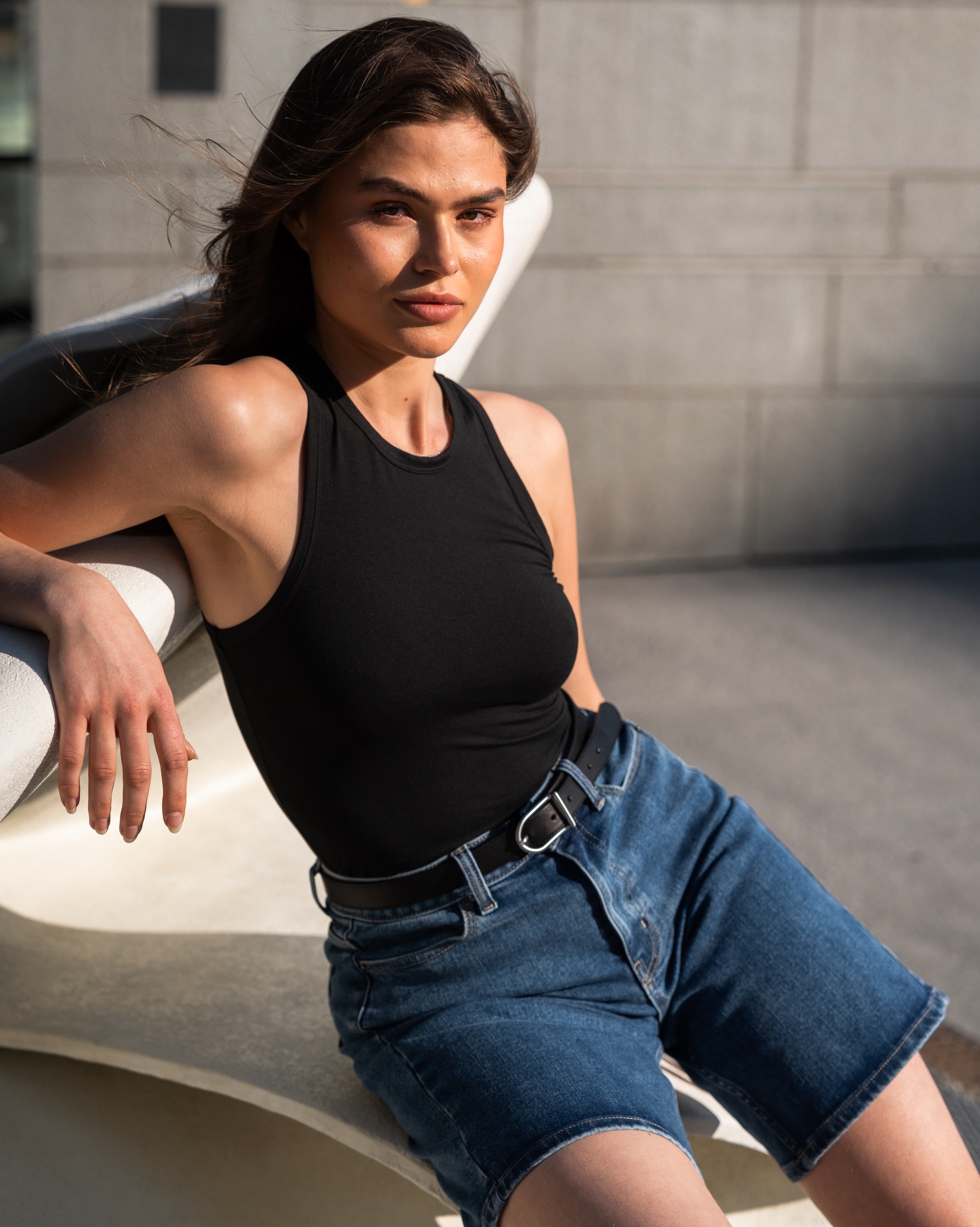 A woman wearing a black Soft Racerback Top styled with mid-blue ComfortDenim shorts and a black belt by Ninepine.